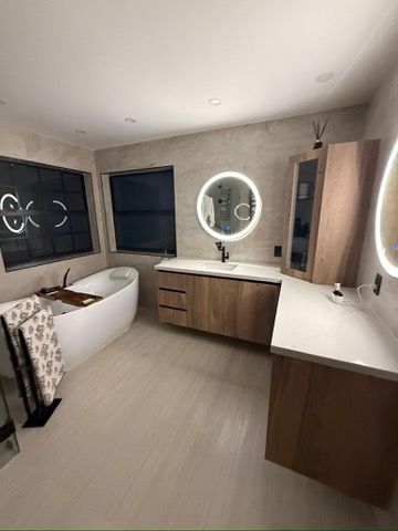 Bathroom with a freestanding tub, round lit mirror and wood vanity